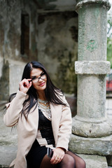 Black hair sexy woman in glasses and coat posed at street of old city.
