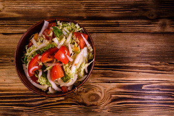 Dietary salad with the chinese cabbage and tomatoes in ceramic bowl on a wooden table. Top view