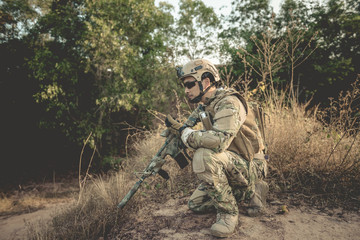 Soldier with gun in had sit in the forest,He's using walkie talkie to call for backup,military in...
