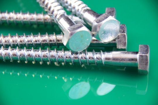 &Uuml;berbelichtet und mit gr&uuml;n reflektierendenm Hindergrund silber schimmernede Sechskantschrauben