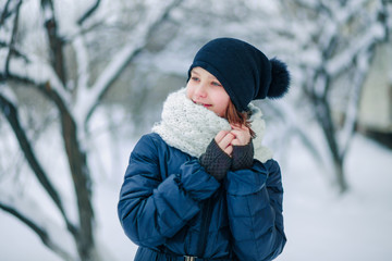 A young girl in a long white scarf on a background of snow-covered branches of trees in the city.