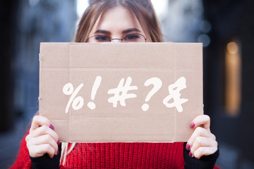 A set of symbols or abuse on a cardboard plate in the hands of a young woman. Disagreement on the online forum or on the Internet.