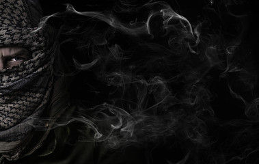 face of a bandit in military uniform on a black background with smoke © Artem
