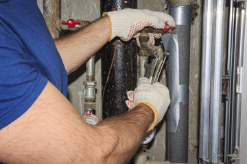 plumber repairs pipes in plumbing unit. Tools plumbing in hand against background of pressure gauges, meters and pipes.
