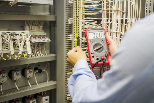 Engineer electrician with multimeter in hands at electric automation box panel. Service engineer tests circuit of industrial equipment