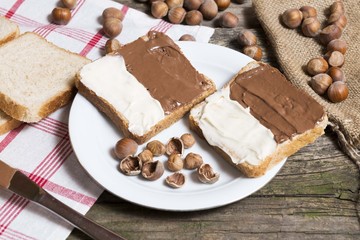 bread slice with nutella chocolated and vanilla cream on wooden table with hazelnuts