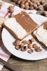 bread slice with nutella chocolated and vanilla cream on wooden table with hazelnuts