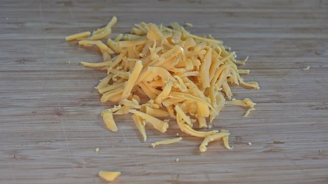 Grated cheddar cheese falling to a cutting board, 4k