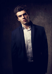 Handsome male model posing in fashion suit and white style shirt looking on dark shadow background....