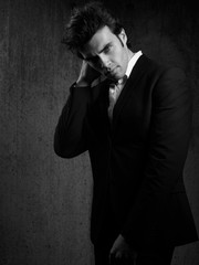 Thinking handsome male model posing in blue fashion suit and white style shirt looking on dark shadow background. Black and white portrait