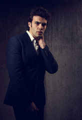 Charismatic handsome male model posing in blue fashion suit and white style shirt looking on dark shadow background.