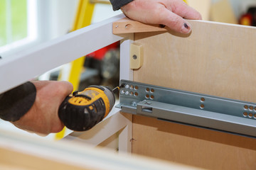 A workman fixing cabinet with screwdriver in kitchen