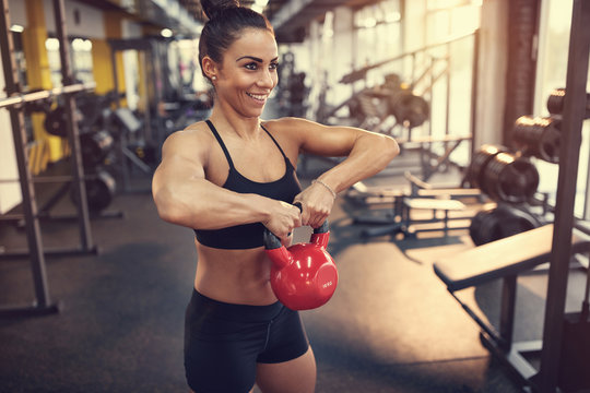 Woman practicing arm muscles with kettle bell weight in gym
