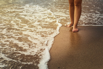 believe and happiness concept of Beautiful bare feet on the sand beach. Sea foam washes female legs Summer time holidays concept Sea waves and sand.