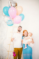 Obraz na płótnie Canvas a young family of three people, mom's dad and daughter's one year old stands inside the room. Holding a balloon in her hand,