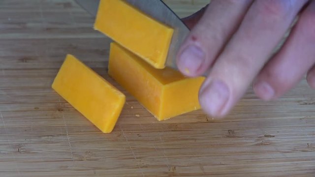Slicing cheddar cheese on a cutting board, 4k