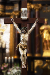 Figure of Jesus Christ hanging on a wooden cross with a faded altar, wreaths and figurines