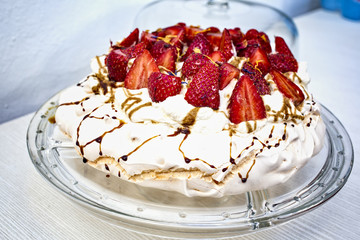 tarta de merengue y fresas cortadas en dos en un plato de cristal transparente y fondo blanco