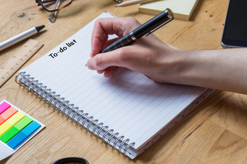 Writing on notepad with to-do list and pen and other accessories on a wooden table from the side