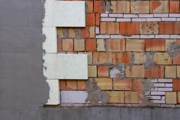 Fragment of a red brick wall during the works connected with the insulation of polystyrene and partly plastered