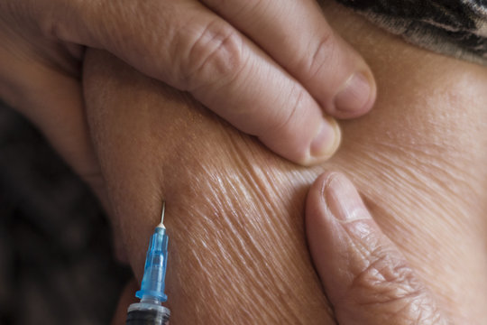 An old woman is injected with a syringe by injecting a medicine into her hand.