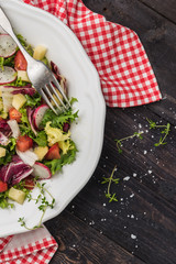 Fresh salad with mixed greens, radish, cheese and tomato in a plate on wooden background. Italian Mediterranean or Greek cuisine. Vegetarian vegan food