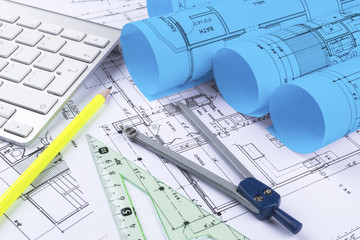 Architectural blueprint drawings of the modern house with computer keyboard. Architectural blueprints and blueprint rolls and a drawing instruments on the worktable. Drawing compass, plans.
