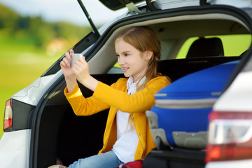 Adorable little girl ready to go on vacations with her parents. Kid taking pictures with her phone in a car.
