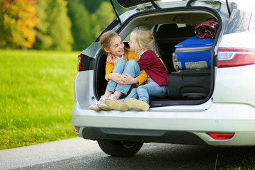 Two adorable little girls sitting in a car before going on vacations with their parents. Two kids looking forward for a road trip or travel.