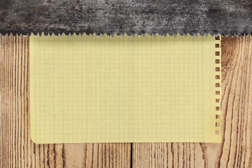 old saw and a piece of notebook on wooden background