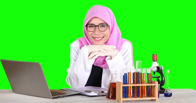 Young female scientist working with laptop computer and test tube on table, smiling at the camera. Shot in 4k resolution with green screen background