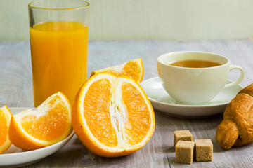 A glass of orange juice, a sliced orange and a cup of tea with a croissant and pieces of cane sugar - a healthy diet concept, a light breakfast
