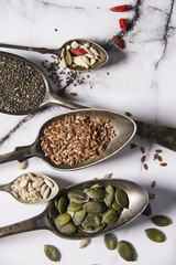 Food ingredients in old steel spoon on marble background. Flax, pumpkin seed, sunflower seed and sesame. healthy food concept
