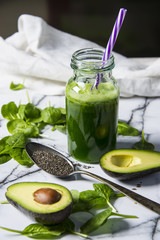 Healthy green smoothie with spinach in a bottle with spinach leaves and fresh avocado on a marble table