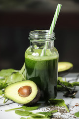 Healthy green smoothie with spinach in a bottle with spinach leaves and fresh avocado on a marble table