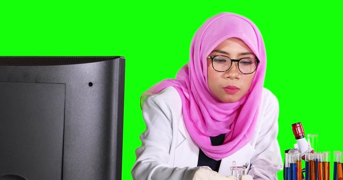 Muslim scientist doing experiment while looking at computer and mixing chemical fluid on test tube. Shot in 4k resolution with green screen background