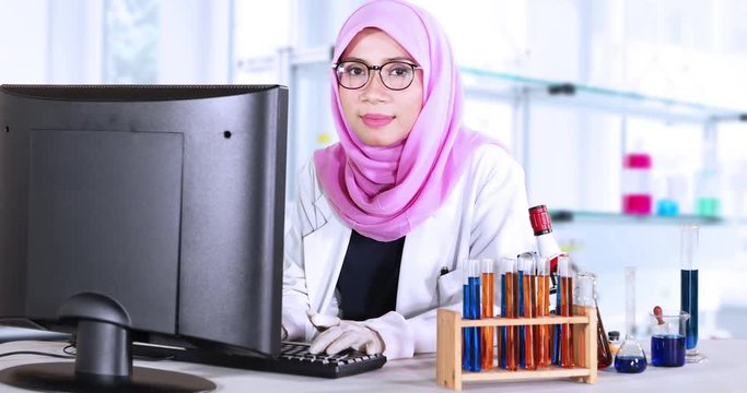 Female muslim scientist working with a computer and smiling at the camera in the laboratory room. Shot in 4k resolution