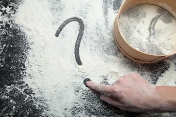  A woman's hand draws a question mark on flour. Sieve for flour and the concept of homemade cakes. © Andrii Zastrozhnov