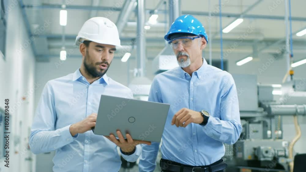 Poster head of the project holds laptop and discusses product details with chief engineer while they walk t