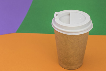Paper cup with coffee on bright orange and green background