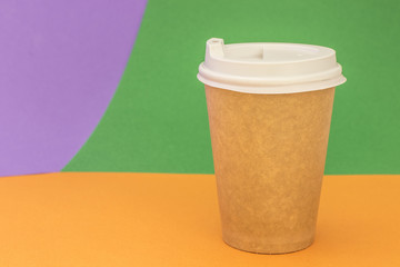 Paper cup with coffee on bright orange and green background
