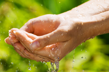 Fototapeta premium Woman washing hand outdoors. Natural drinking water in the palm. Young hands with water splash, selective focus