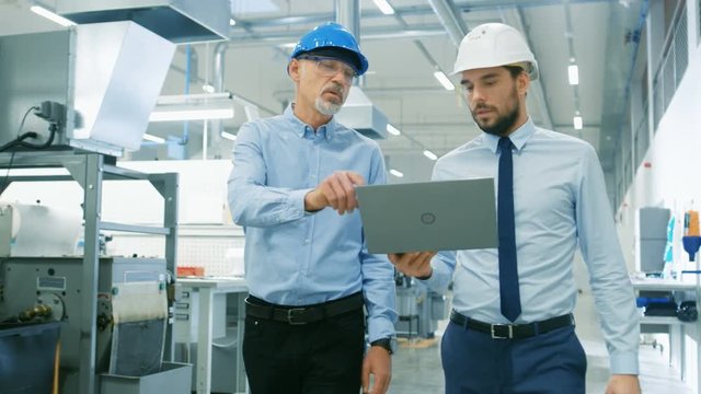 Head of the Department Holds Laptop and  Discuss Product Details with Chief Engineer while They Walk Through Modern Factory. Medium Shot.
 Shot on RED EPIC-W 8K Helium Cinema Camera.