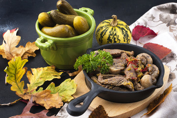 fried meat with mushrooms in a frying pan. on a black background