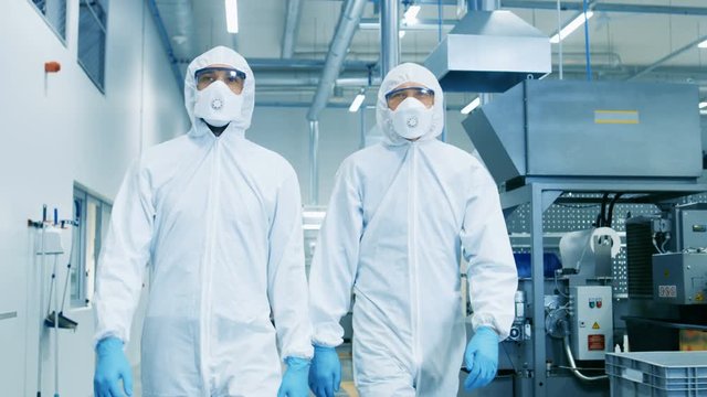Two Engineers/ Scientists in Hazmat Sterile Suits Walking Through Technologically Advanced Factory/ Laboratory. Clean High-Tech Environment with CNC Machinery. 