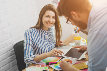 Beautiful young designers discussing ideas and smiling while working in office
