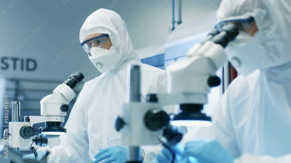 Poster two engineers/ scientists/ technicians in sterile cleanroom suits control manufacturing machinery wo