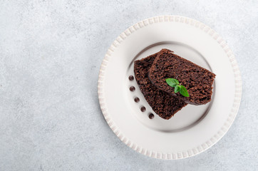 Two slices of chocolate cake with mint leaves served on a white