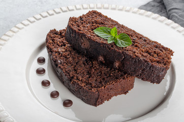 Two slices of chocolate cake with mint leaves served on a white