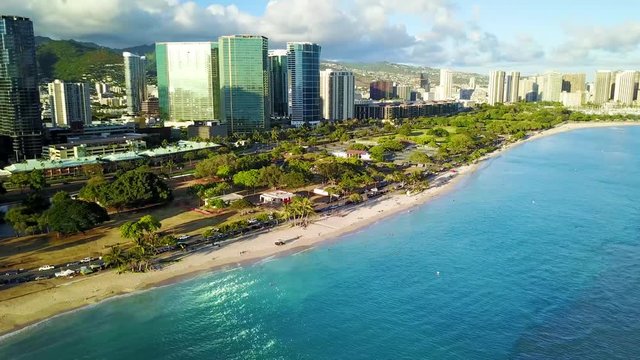 Aerial View: Ala Moana Beach Park Near Magic Island Lagoon In Waikiki. Blue Ocean Water With Condos And Hotel Buildings Nearby. Calm Gentle Water Lapping On White Sand Beach.  Tourist Vacation Spot.